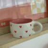 A coffee mug with hearts on it is on a shelf.